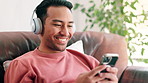 Phone, headphones and man on sofa at apartment networking on social media, mobile app or internet. Smile, typing and male person listening to music, radio or album on cellphone in living room at home