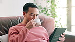 Tablet, coffee and man relaxing on couch for social media, streaming video or browsing internet in living room. Technology, smile and male person with caffeine for happiness, peace or reading blog