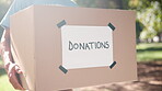 Donation, box and giving to charity with hands on container of clothes or food to giveaway to poor community. Offer, support and volunteer person in nonprofit helping outdoor with cardboard package