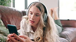 Woman, headphones and music with cellphone on couch, singing and update on social media in home. Young person, streaming and mobile app for online radio with subscription, relax and weekend on sofa