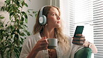 Woman, headphones and coffee break with podcast, relax and rest at home or apartment living room. Lady, window and smartphone for learning, knowledge and story or information for happiness on sofa