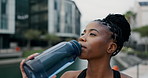 Training, fitness and black woman drinking water in a city for running, exercise or outdoor cardio routine. Sports, liquid and African female runner with drink for workout, hydration or body recovery