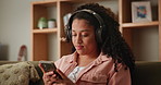 Girl, home and sofa on smartphone with headphone for music playlist and smile for entertainment. Female person, lounge and couch on internet for streaming service or social post and online video.

