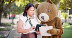 Business people, tablet and discussion of team outdoor with documents at park in funny teddy bear costume. Tech, paperwork and collaboration of consultants planning with woman and mascot in garden