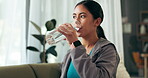 Fitness, drinking water and asian woman on sofa after training, exercise and workout for wellness in living room. Bottle, hydration and female person for energy, clear liquid or aqua in home gym