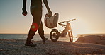 Motorcycle, helmet and person walking at sunset to travel in extreme sport and outdoor adventure. Motorbike, safety and driving on hill at beach with protection for transport, journey or training