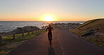 Person, road and motorbike with sunset for travel, adventure or riding with training in extreme sports. Back of a biker with safety helmet and bike for journey coast, ocean or sea and road in summer