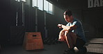 Break, exercise and time with sports man in gym to rest for recovery from training or workout fatigue. Fitness, health and watch with tired young athlete sitting to relax in performance center