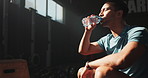 Break, fitness and water with sports man in gym to rest for recovery from training or workout fatigue. Exercise, health and drink with tired young athlete sitting to relax in performance center
