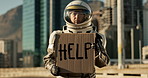 Astronaut, city and billboard with sign for help, message or alert of signal, news or note to people on earth. Portrait of traveler with board for notification, awareness or protest in an urban town