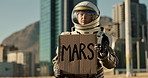 Astronaut, city and billboard with mars sign for travel, message or note to people on earth. Space traveler showing board, poster or notification for alert, signal or awareness in an urban town
