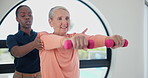 Physiotherapist, senior woman and dumbbells for exercise with care, muscle or wellness at fitness clinic. People, physical therapy and helping hand for rehabilitation, injury and training for arms
