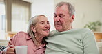 Senior, couple and laughing with hug on sofa for bonding, retirement and conversation in living room of home. Elderly people, coffee and embrace on couch with romance, wellness and morning break