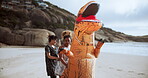 Funny, people and dinosaur with costume for playing in beach or ocean, happiness and joy of women together. Outdoors, animal and girls moving or excited for comedy, entertainment or cheerful dance