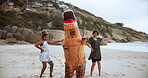 Funny, people and dinosaur with costume for dancing in beach or ocean, happiness and joy of women together. Outdoors, animal and girls moving or excited for comedy, entertainment or cheerful dance