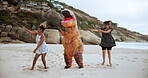 Fun, people and dinosaur with costume for dancing in beach or ocean, happiness and joy of women together. Outdoors, animal and girls moving with excitement for comedy, entertainment or cheerful dance