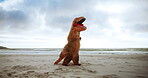 Dinosaur, costume and play with fun in beach, comic and silly with mascot, funny and outdoor. Nature, entertainment and goofy, person and comedy in sea, environment and inflatable suit and blue sky