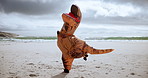 Comic, funny and dinosaur costume on beach dancing with energy for comedy joke on vacation travel. Goofy, silly and inflatable animal mascot moving, jumping and having fun by ocean on holiday.