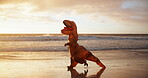 Costume, dinosaur and person running on beach at sunset for cardio, comedy or fitness in summer. Exercise, nature and wellness by ocean with adult athlete in t-rex outfit for workout as runner
