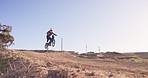 Motorbike, jump and person in off road sport in desert, sand with path on hill for stunt challenge. Dirt, trail and driver travel on motorcycle with skill, technique and moto adventure in countryside