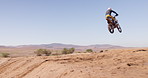 Dust, sand and bike in sports for stunt, adventure or adrenaline with desert in countryside. Motorcycle, freedom and athlete fearless for speed, challenge or fast jumping by hill, outdoor or nature