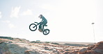 Jump, motorbike and biker in air or outdoor training for extreme sports, safety and practice on sand. Sky, risk or fearless person flying on motorcycle for off road race, hill or trick in challenge