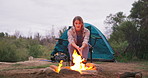 Fire, woman and camping wood with flames for heating hands and calm in nature with a tent. Adventure, field and rocks in a campsite with smoke, burning and pit with travel and holiday in a park