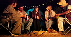 Camping, night and friends drinking by fire outdoor in nature for adventure, bonding or getaway together. Travel, happy and dark with group of happy young people talking on holiday or vacation