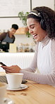 Woman, phone and headphones in coffee shop for texting, laughing and funny meme on internet in diner. Girl, person or freelancer on break from remote work, comic video and notification in cafeteria