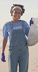 Woman, face and volunteer with plastic bag on beach for cleaning as community activist, earth day or conservation. Female person, wind and ngo clean up or waste management, pollution or recycling