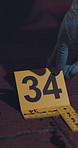 Person, hands and crime scene with number for evidence, investigation or markings on floor at night. Closeup of forensic investigator with point for scale, comparison or photograph of blood or murder