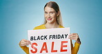 Face, Black Friday or happy woman with sale sign for discount deal, offer poster or launch ads. Wink, smile or person with board for message, marketing or promotion card on blue background in studio