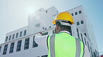 Black man, construction and safety helmet pointing at building in city for industrial architecture on site. African male contractor, engineer or architect inspection for architectural detail in town