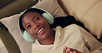 African woman, headphones and above on sofa with smile, relax and singing with music in home living room. Girl, listening and happy for streaming, audio subscription or lying on lounge couch in house