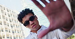 Man, fashion and frame of hand in city for urban style, confidence and designer outfit. Male person, serious and sunglasses with gesture by buildings for trendy, clothes and streetwear in low angle