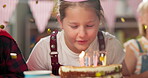 Girl, cake and blowing candles at birthday party with applause, celebration and confetti with friends. Child, happy and fun with event, surprise and hat in home with enjoyment, memory and dessert