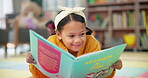 Girl, school and reading book in class, childhood development and growth for vocabulary in kindergarten. Happy, smile and knowledge or information with storybook, learning and fantasy for child