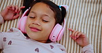 Headphones, smile and girl child on bed dancing to online music, radio or playlist at home. Happy, rest and kid streaming song or album on internet with technology in bedroom at house from above.
