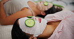 Women, face mask and skincare with cucumber for relax on bed, skin glow and acne treatment. Friends, facial product and fruit for cosmetic on floor with zen health, spa and vegan beauty from above