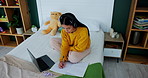 Girl, student and writing with laptop on bed for homework, study or online assignment at home. Female person, teenager or learner taking notes in bedroom for exam, test or learning with headphones