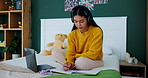 Girl, student and writing with laptop or book on bed for homework, study or online assignment at home. Female person or learner taking notes in bedroom for exam, test or learning with headphones