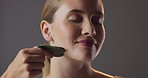 Smile, skincare and woman in studio with gua sha for natural beauty, massage and luxury cosmetics. Dermatology, facial care and girl with confidence, jade stone and healthy skin on grey background.