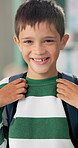 Student, boy and happy with backpack in classroom for education, back to school or ready for knowledge. Scholar, portrait or excited face at preschool with confidence for learning, studying or lesson