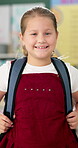 Student, girl and face with backpack in classroom for education, back to school and ready for knowledge. Scholar, portrait and excited at preschool with confidence for learning, studying and lesson