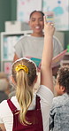 Question, hand up and children in classroom for answer in lesson, learning and education. Teacher, school and group of young boy and girl students in reading session for asking, feedback and studying