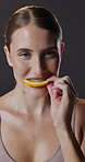 Beauty, eating orange slice and woman in studio on dark background for dermatology or vitamin c. Portrait, skincare and smile with happy model biting citrus fruit for diet, health or nutrition