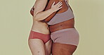 Body positivity, studio lingerie and women hug, care and support different shape, size or fashion inclusivity. Closeup, friends and hugging with lingerie panty, bra and solidarity on green background