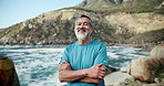 Senior man, runner and arms crossed with smile on face by ocean for training, fitness and health. Asian person, happy and outdoor for exercise, workout and portrait on rocks with wind in summer