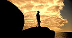 Person, silhouette and orange sky background with cloud cover for relax, peace and freedom. Man, shadow and nature with ocean waves, rocks and sunset for motivation, hike adventure and wellness