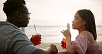 Couple, drinks and bench talking on date for love, relationship or communication in summer sunset. Together, man and woman happy with beverages for vacation, holiday and travel with beach view